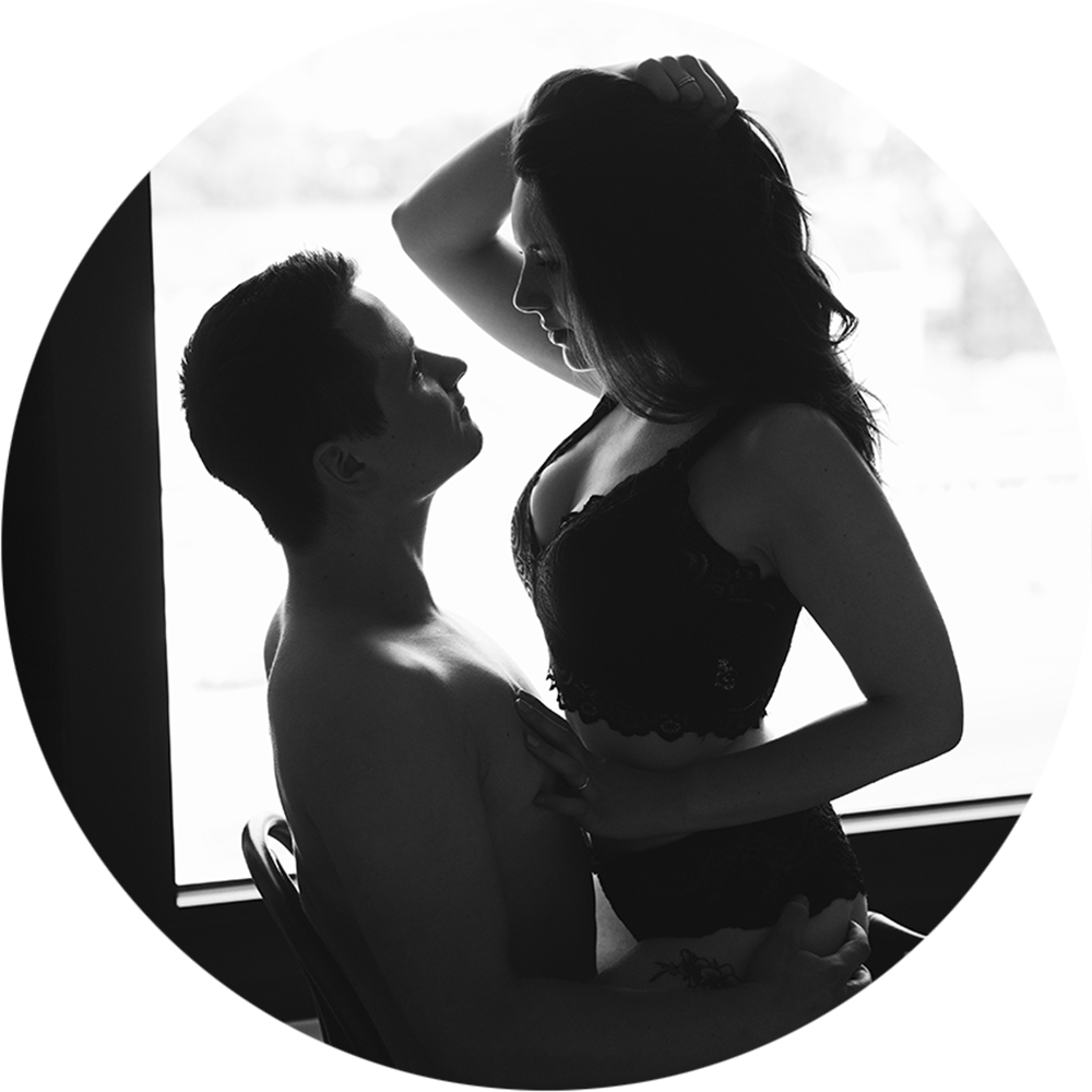 Paar sitzt in aufreizender Pose auf einem Stuhl vor einem Fenster für ein Couple Boudoir Fotoshooting